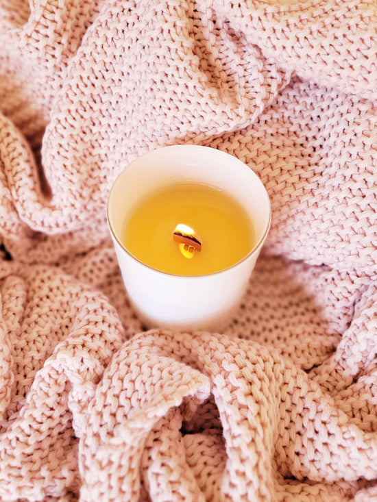 An Ebb & Flo candle, with wooden wick lit, encased in a pink blanket